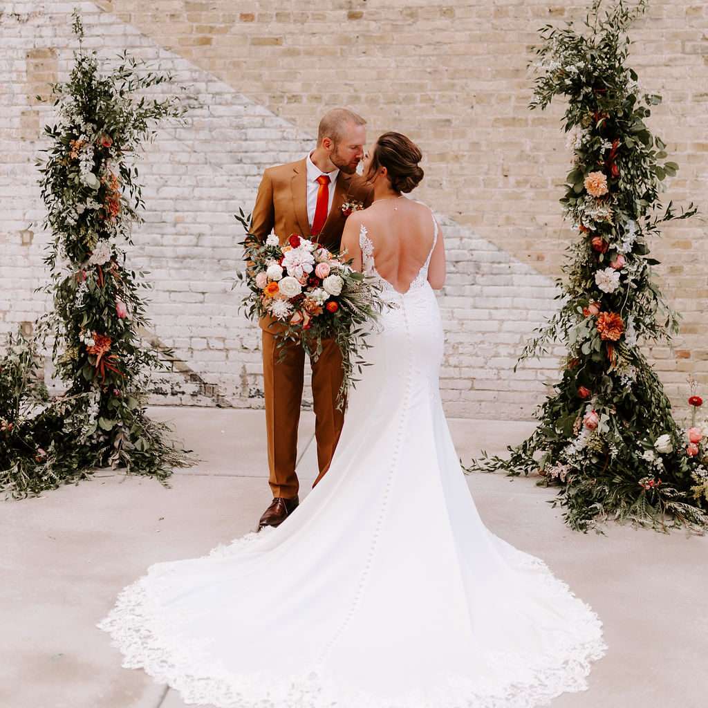 Newlyweds pose in front of the brick wall in The Urb Garden at Mercantile Hall.