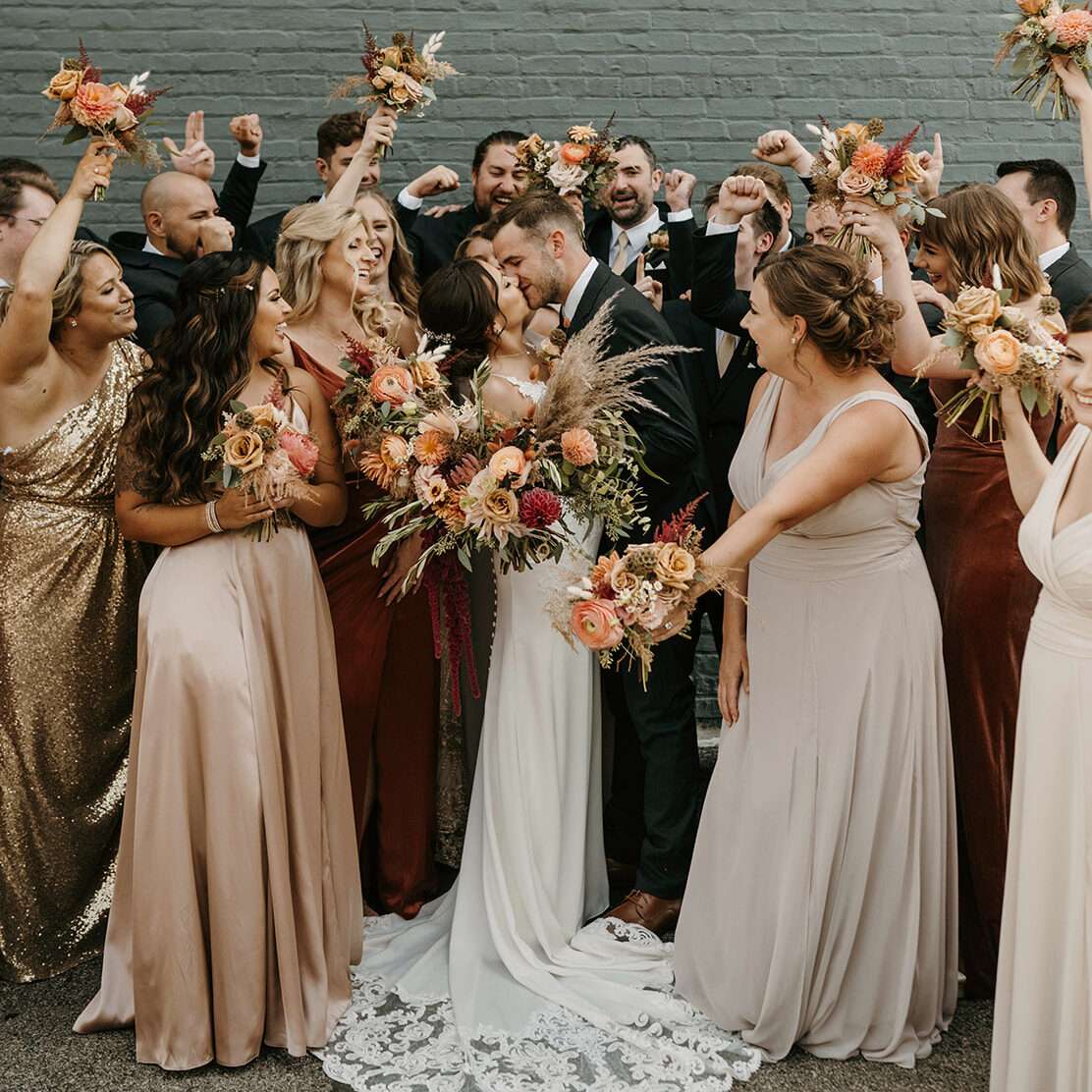 Newlyweds celebrating with their wedding party in front of Mercantile Hall's green wall.