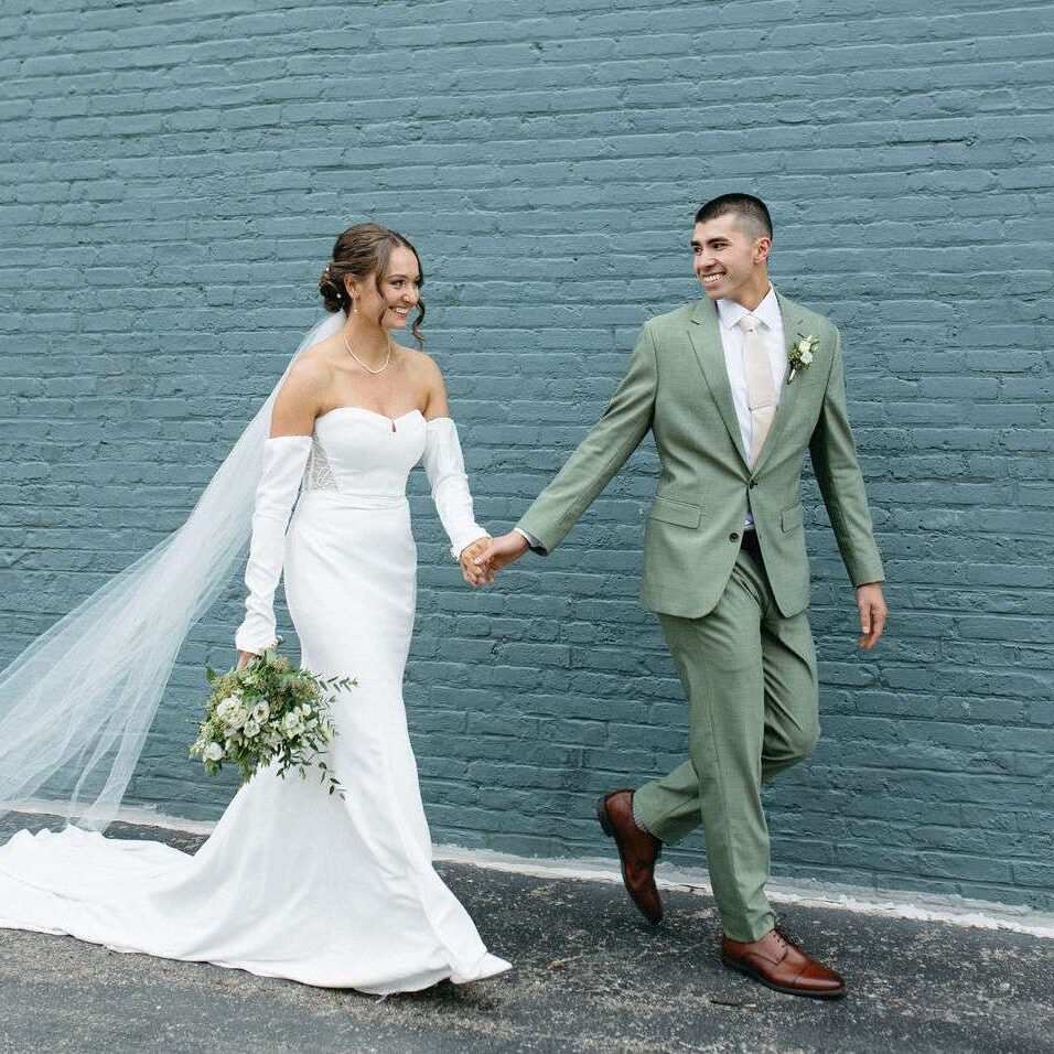 Newlyweds walk in front of Mercantile Hall's green wall.