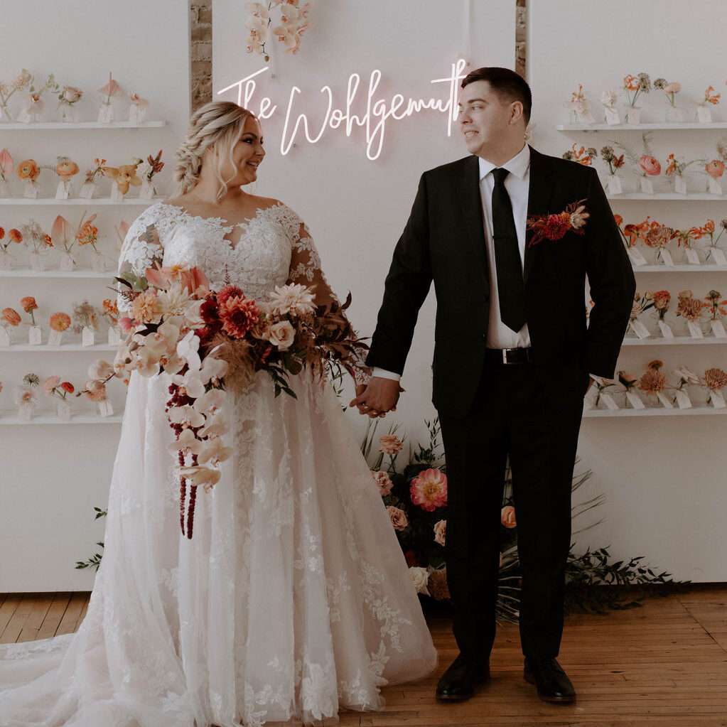 Newlyweds pose by their escort card wall display at Mercantile Hall.