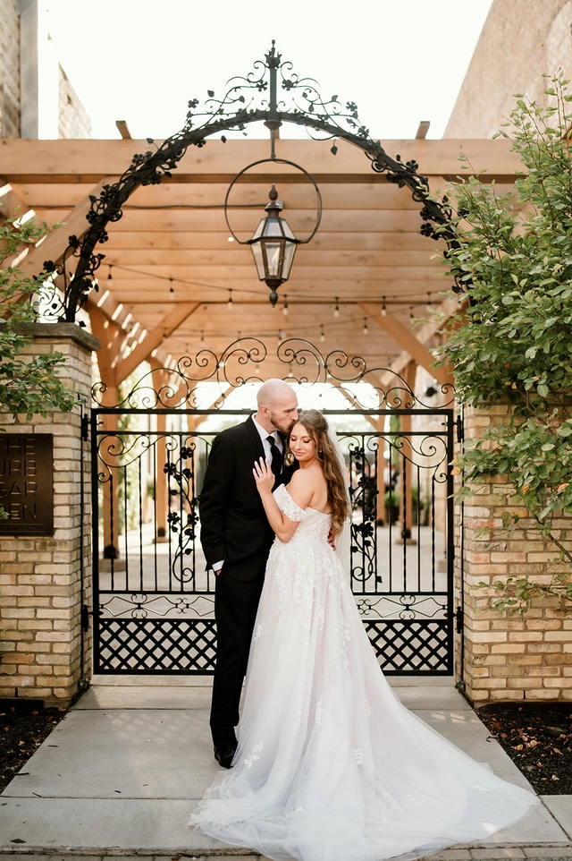 Bride and groom embracing under arched wrought iron gate at Mercantile Hall courtyard