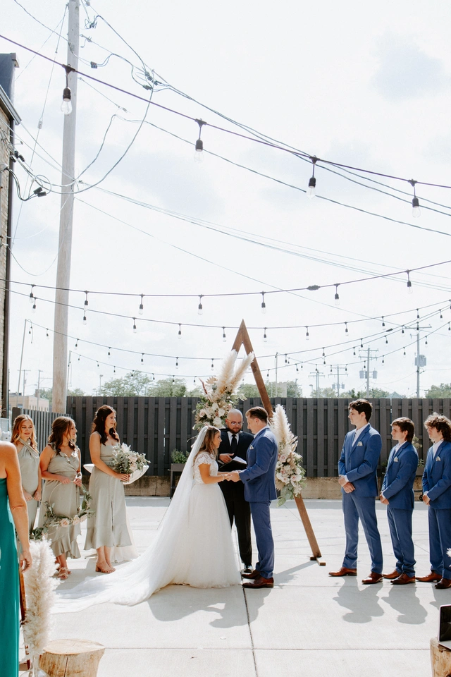 Bride and groom exchange vows under triangle arch in Mercantile Hall’s outdoor courtyard