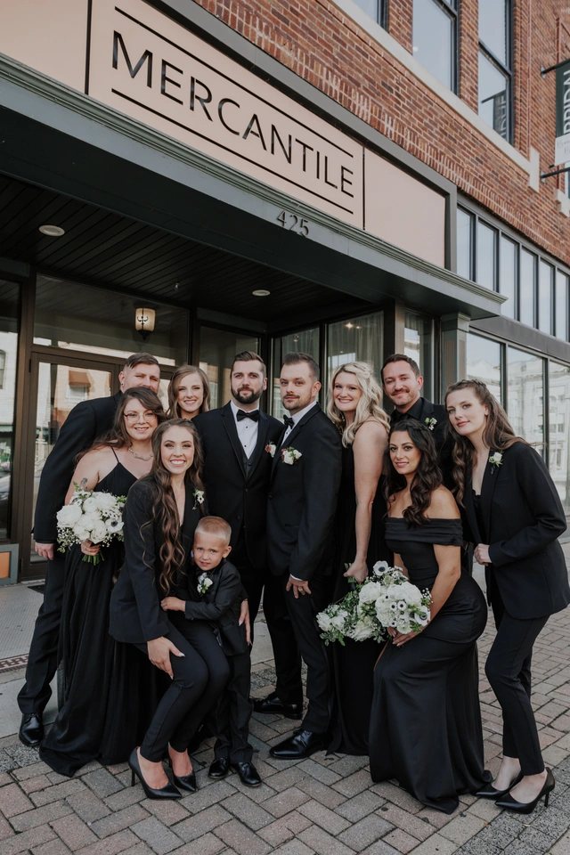 Wedding party in all-black attire poses outside Mercantile Hall's front entrance in Burlington, Wisconsin