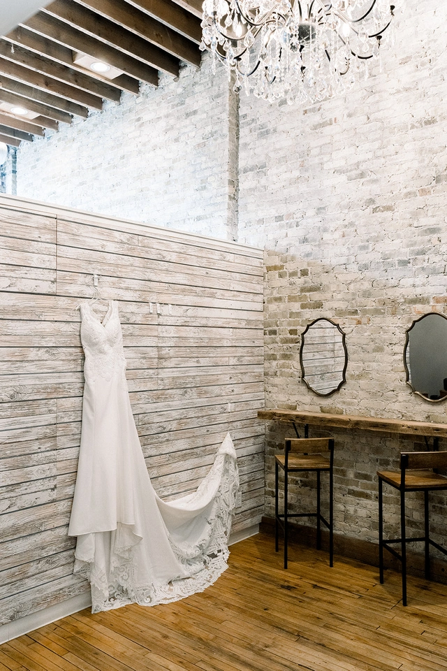 Lace wedding dress hanging in rustic bridal suite with wood and brick walls