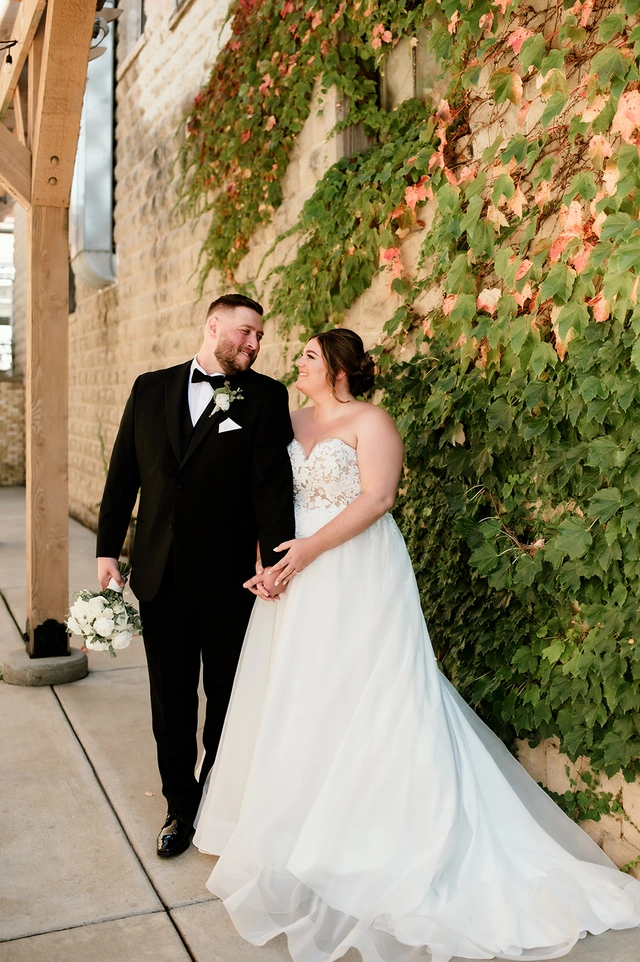 Bride and groom walking hand in hand beside ivy-covered brick wall at Mercantile Hall