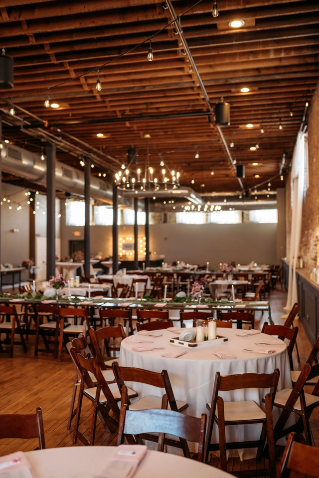 Wide view of a wedding reception setup inside Mercantile Hall with round tables and string lights