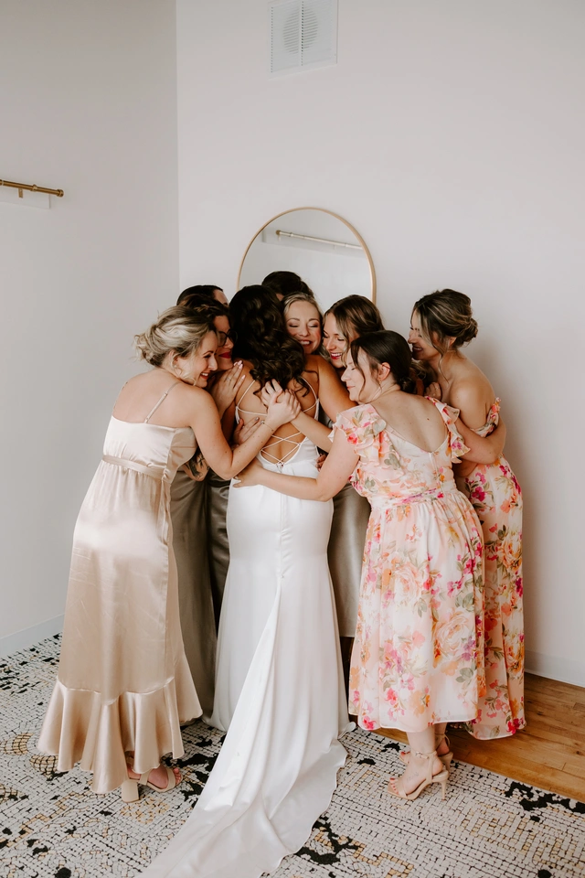 Bride in modern white gown shares an emotional group hug with bridesmaids in the Loft at Mercantile Hall