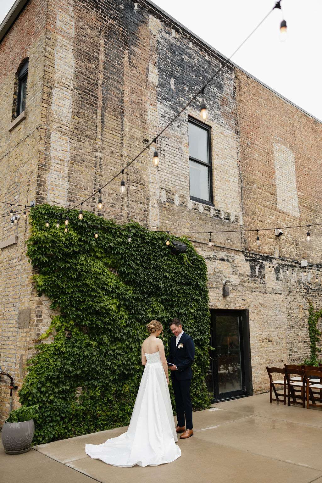Bride and groom holding hands near ivy-covered brick wall at Mercantile Hall courtyard