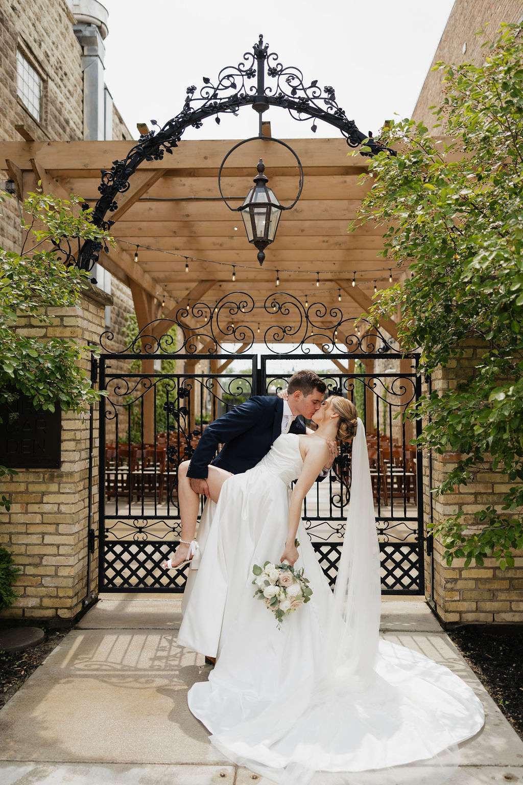 Groom dips bride for a kiss under the pergola and black iron gate at Mercantile Hall in Burlington, WI