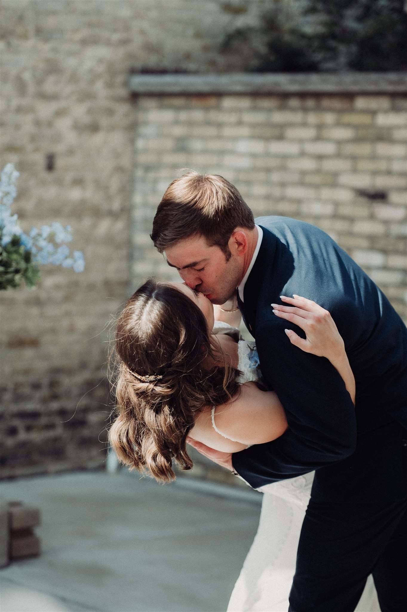 Bride and groom share a close-up dip kiss outdoors against a brick wall