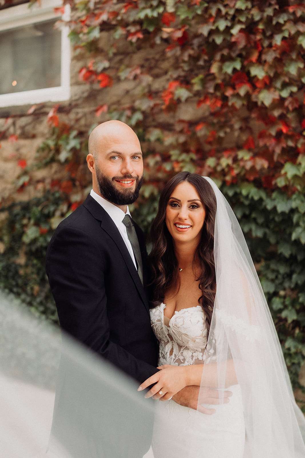 Bride and groom smiling in front of an ivy-covered wall during fall at Mercantile Hall