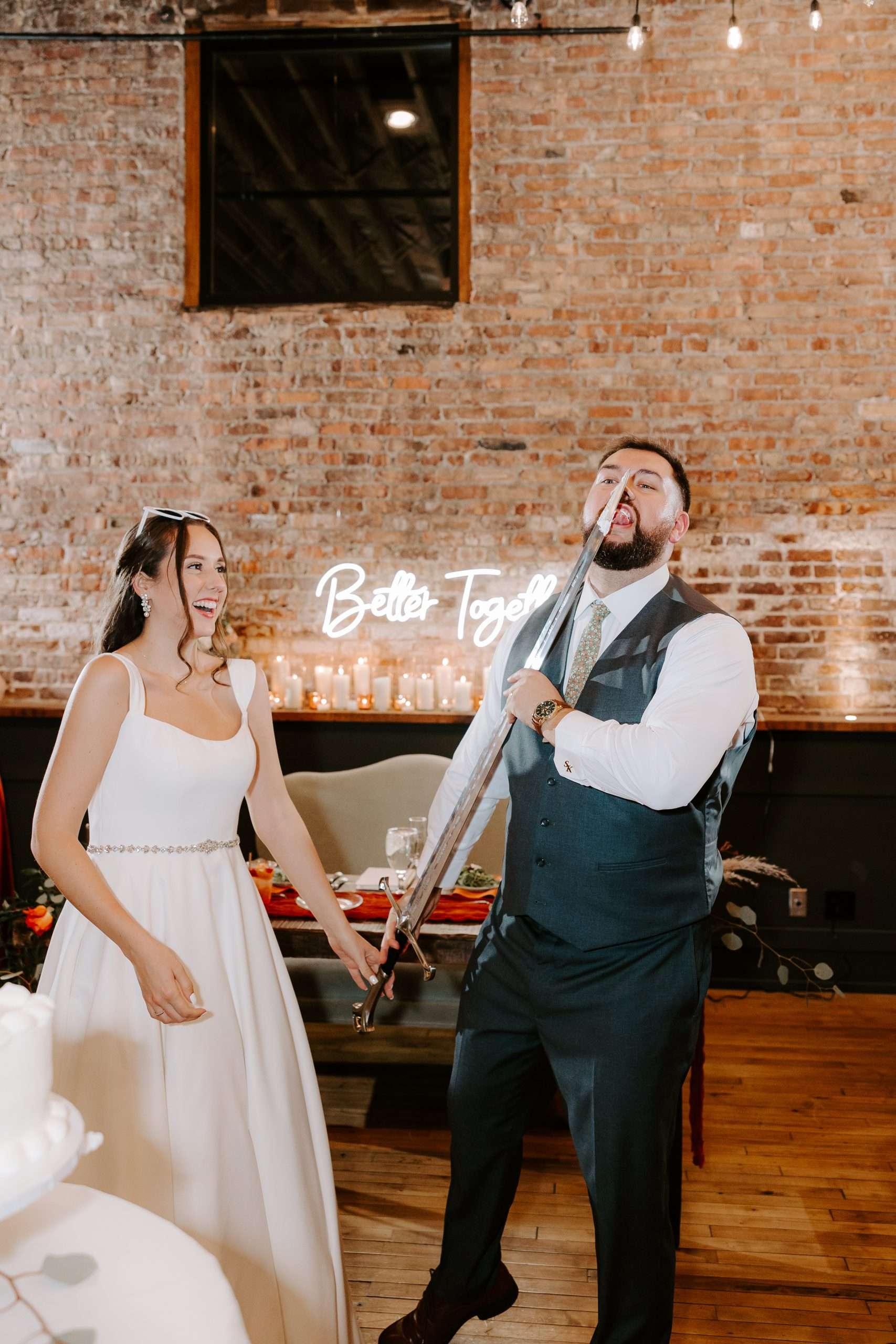 Bride and groom laugh as the groom pretends to eat wedding cake with a giant sword in a fun reception moment