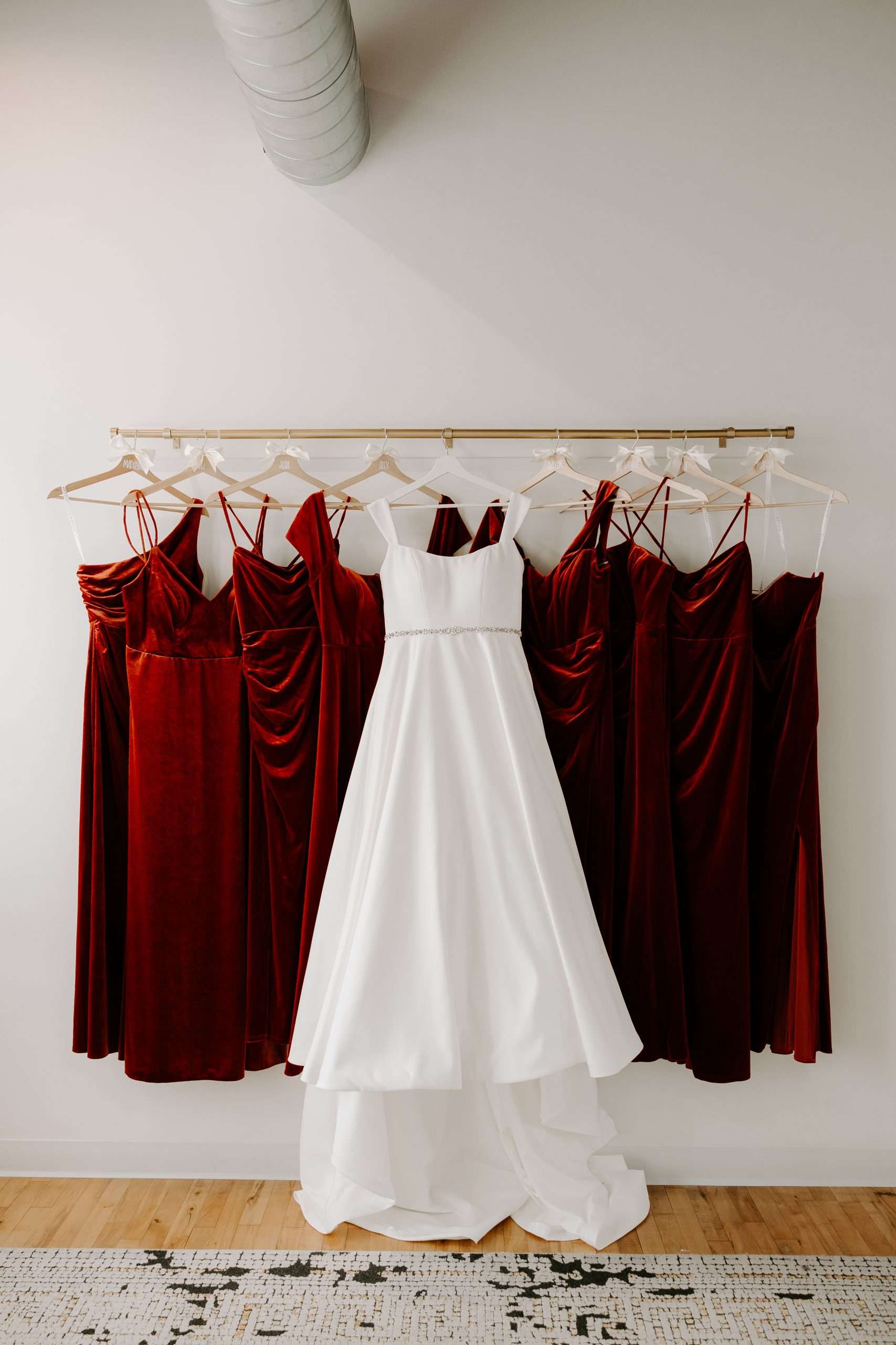 White wedding dress and burgundy velvet bridesmaid dresses hanging in bridal suite at Mercantile Hall