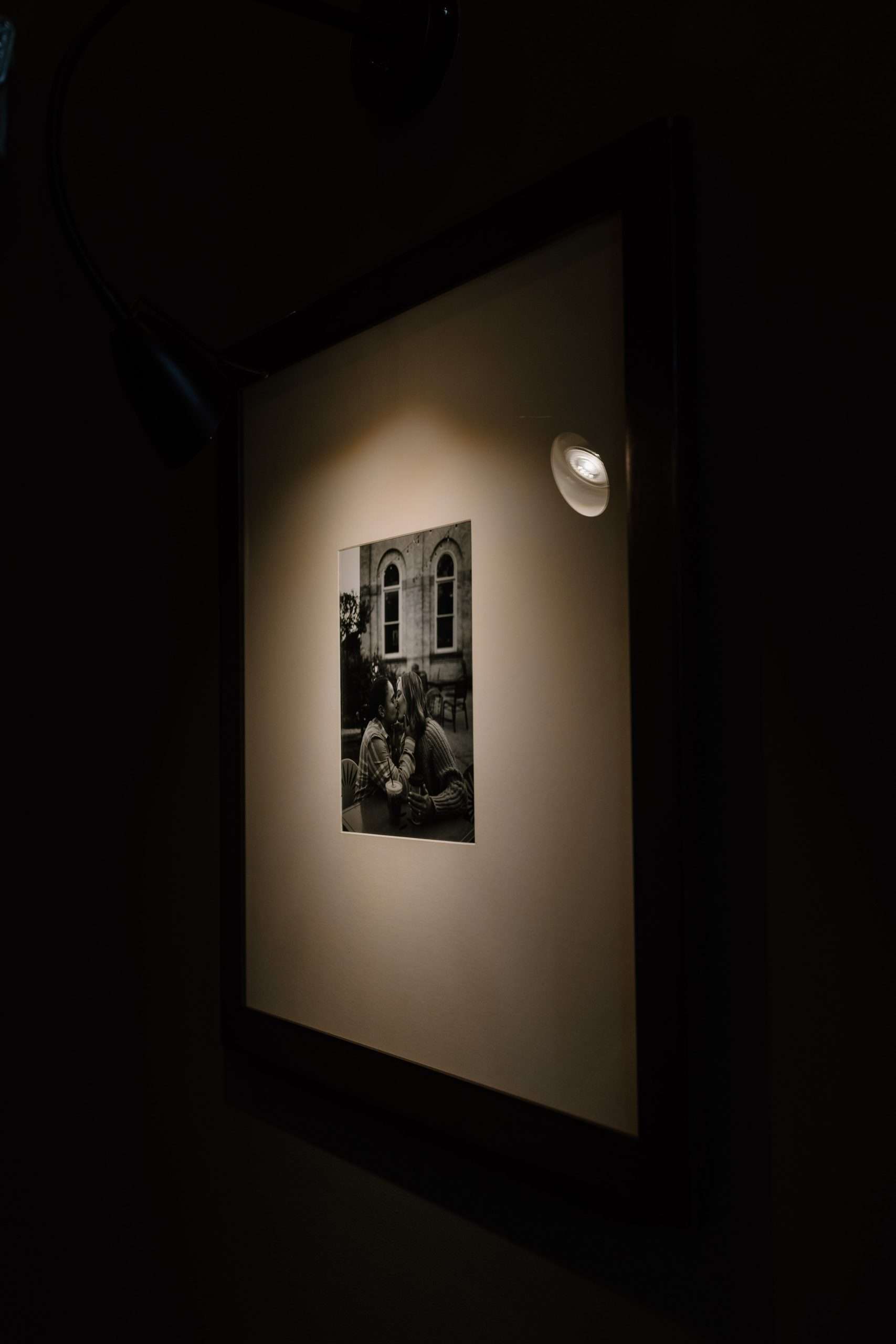 Framed black-and-white photo of a couple kissing outdoors, illuminated by a single spotlight against a dark wall