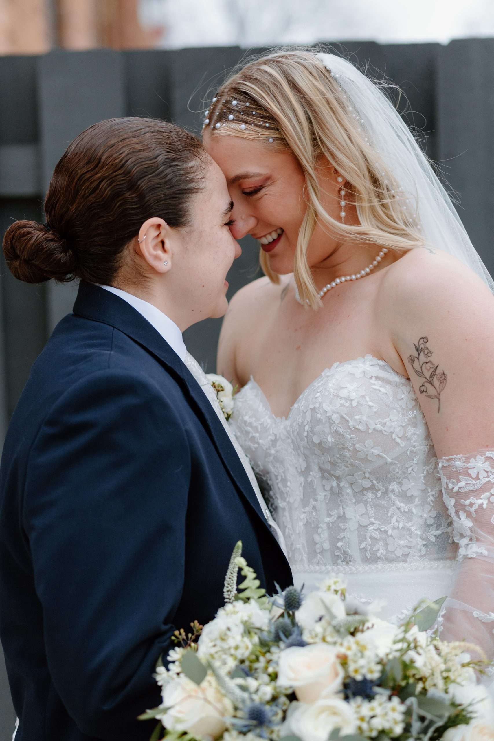 Intimate wedding portrait of bride and partner forehead-to-forehead, smiling and holding a lush white and green bouquet