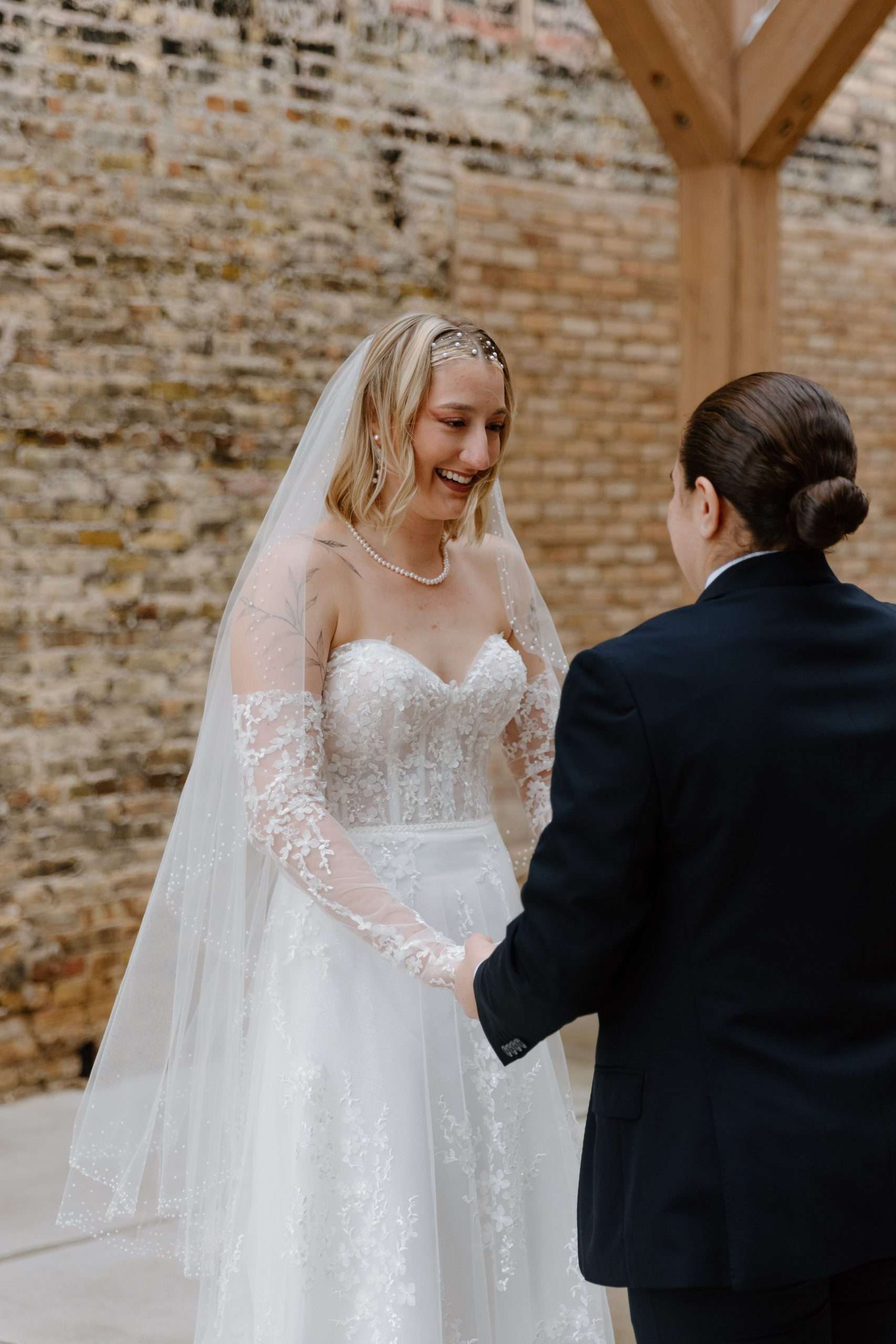 Bride and groom holding hands and smiling during their outdoor wedding ceremony in front of a rustic brick wall