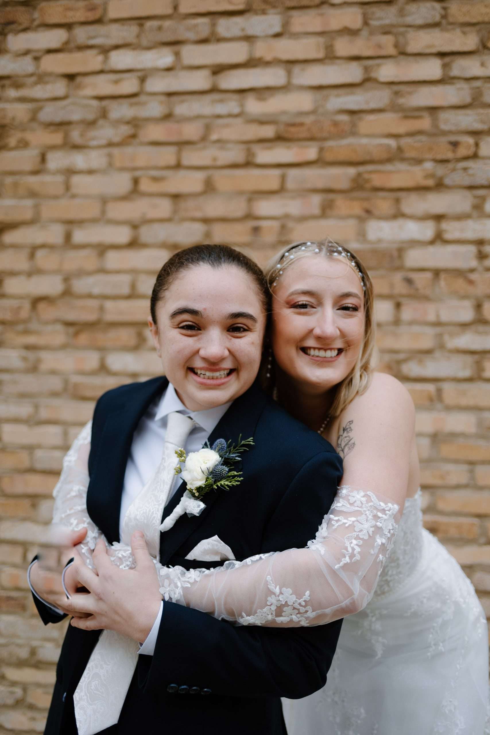 Smiling newlywed couple hugging happily outdoors with rustic brick wall background