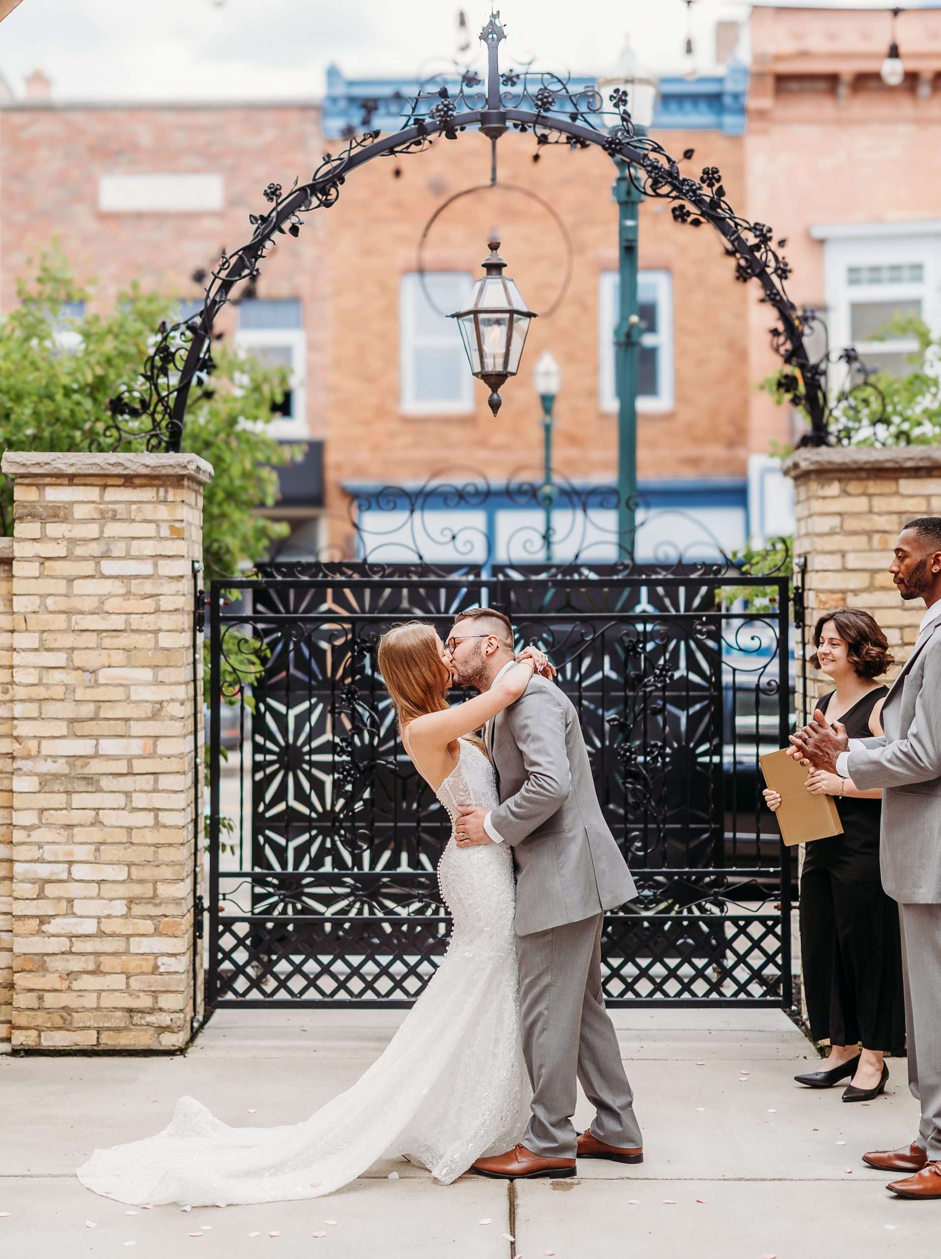 Bride and groom kissing under wrought iron arch during outdoor wedding ceremony at Mercantile Hall in Burlington, WI