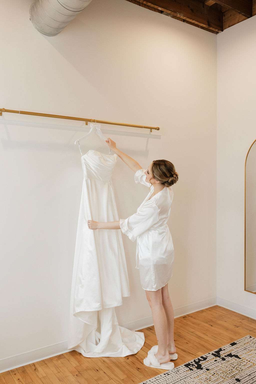 Bride in robe admires her wedding gown hanging in the Loft suite at Mercantile Hall