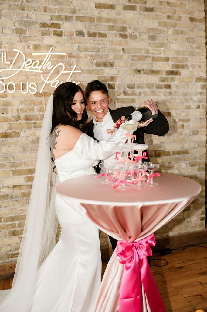 LGBTQ+ couple pouring champagne into a tower at their Southern Wisconsin wedding at Mercantile Hall
