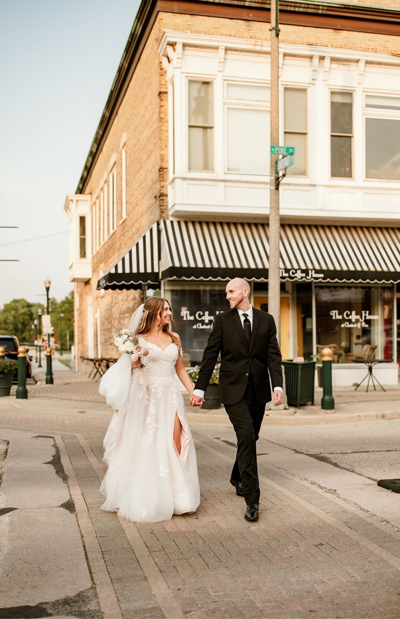 Wedding couple walking close together beside storefront windows in downtown Burlington, Wisconsin, their reflections visible in the glass.
