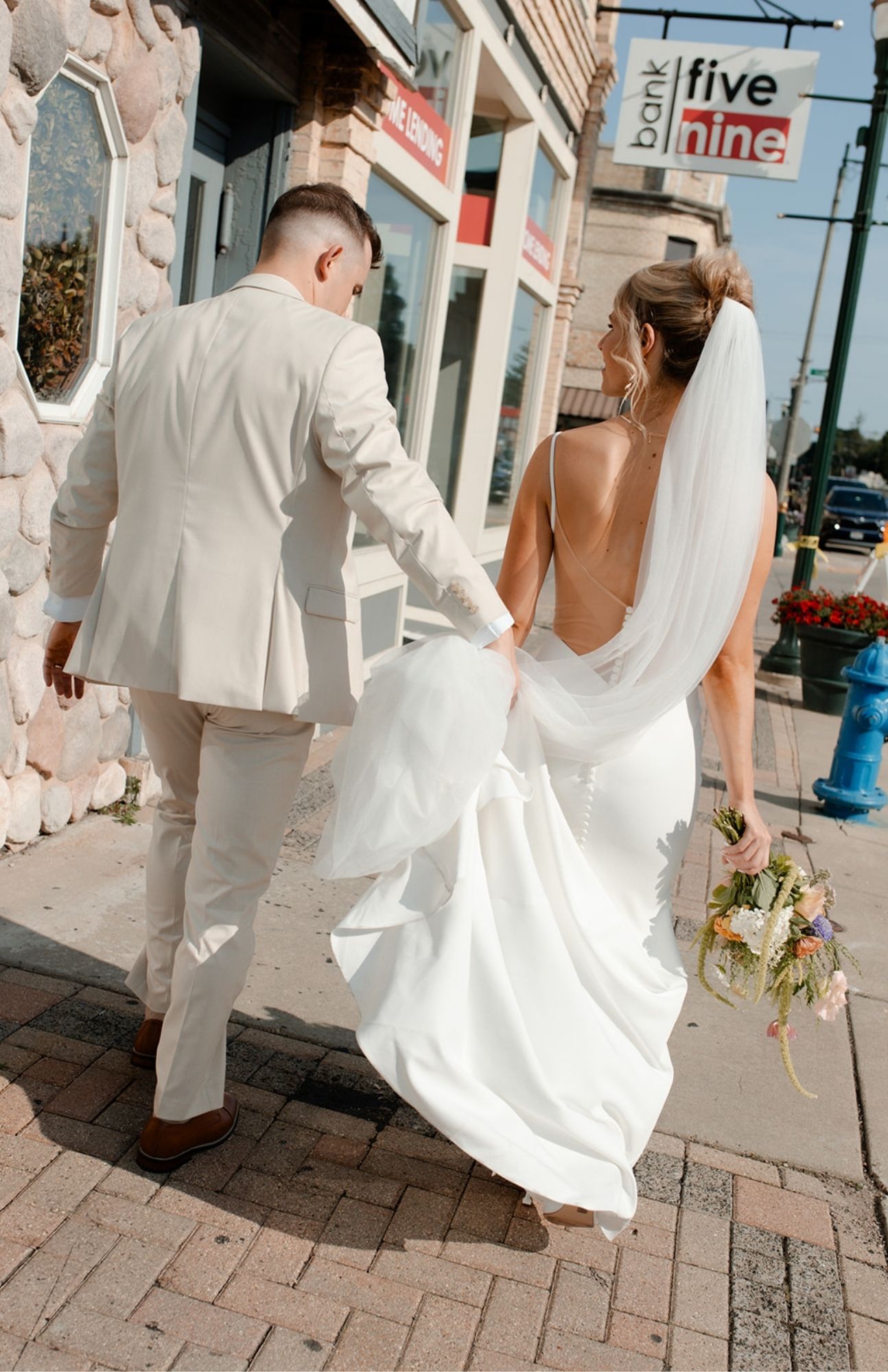 Bride in a flowing gown and groom in a tailored suit walking toward Mercantile Hall on a quiet downtown Burlington street